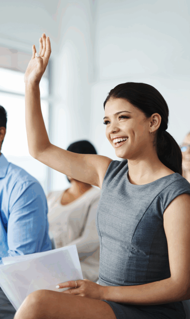 Smiling woman raising her hand in a group setting, representing empowered women ready to seek clarity and take aligned action through coaching with Dr. Ashley.