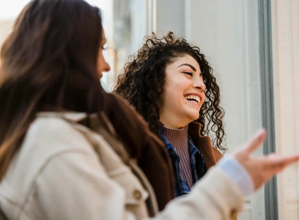Two women smiling and engaged in expressive conversation, representing personal empowerment and reclaiming one’s voice and desires through coaching with Dr. Ashley.