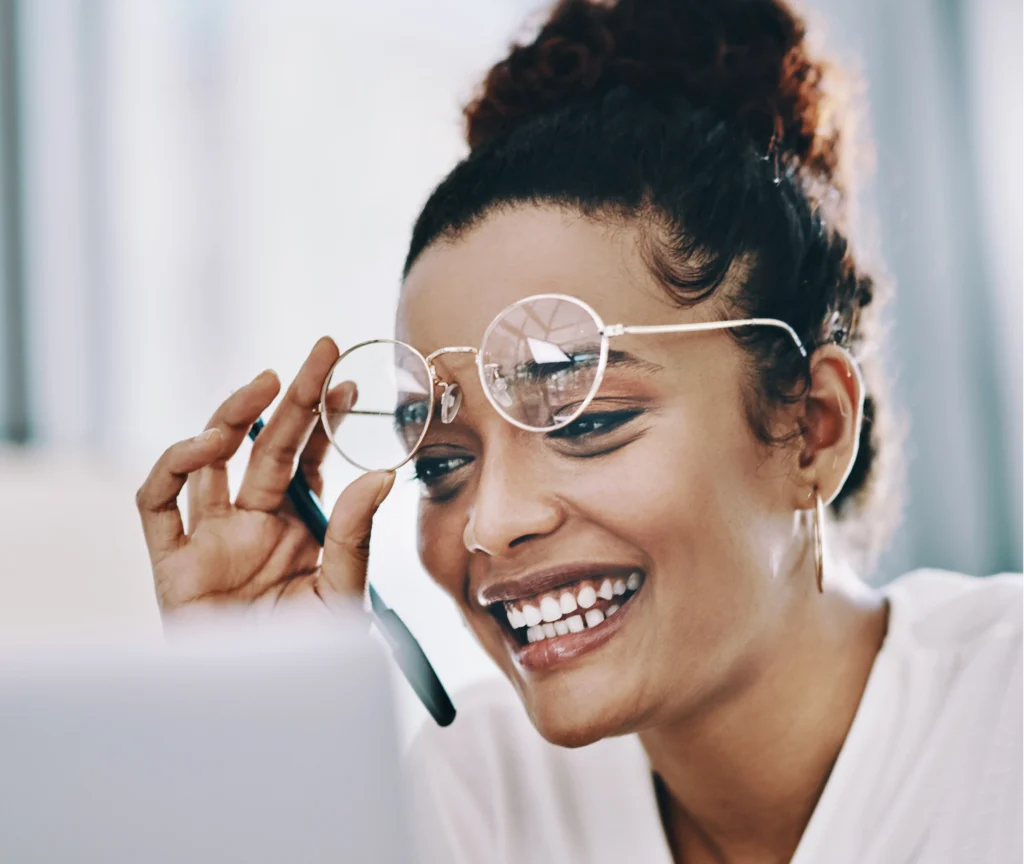 Smiling woman with glasses looking at a laptop during a coaching session, representing clarity, warmth, and connection in a 1:1 Clarity Call with Dr. Ashley.