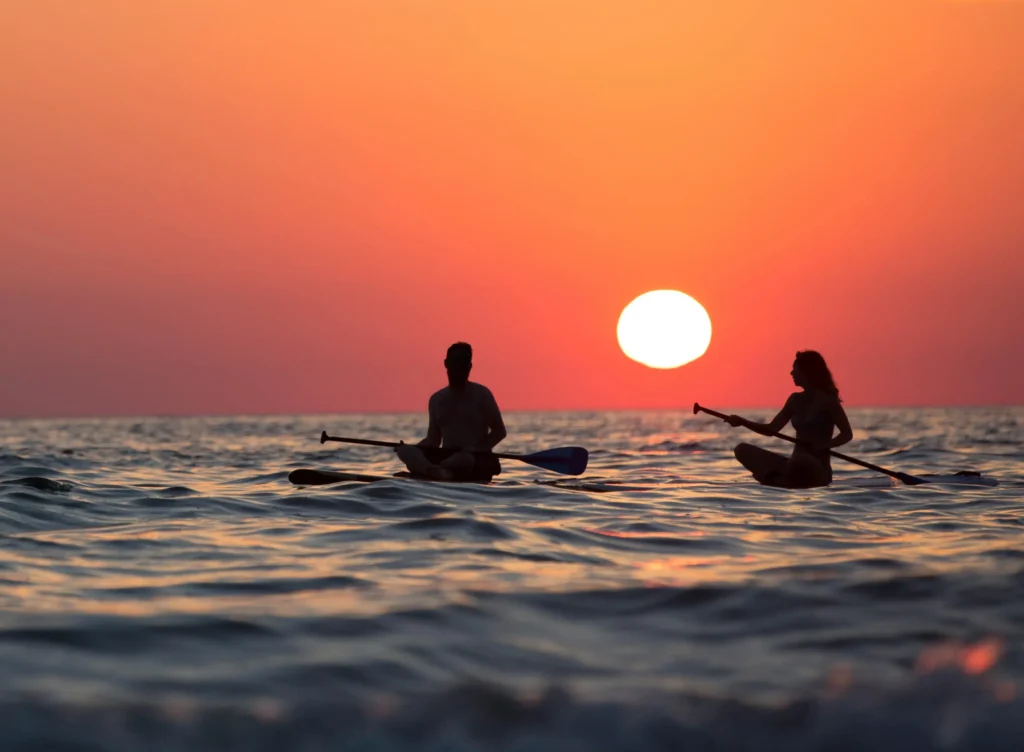 Silhouetted couple paddleboarding at sunset, symbolizing harmony, connection, and a new way of relating through coaching with Dr. Ashley.