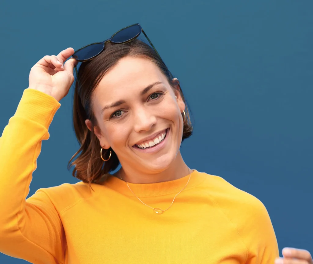 Confident woman smiling in a vibrant yellow top against a teal background, symbolizing radiance and personal empowerment