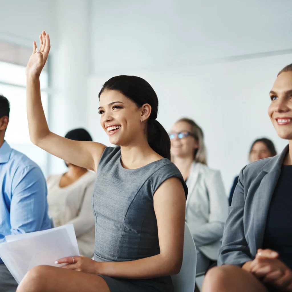 Smiling woman raising her hand in a group setting, representing empowered women ready to seek clarity and take aligned action through coaching with Dr. Ashley.